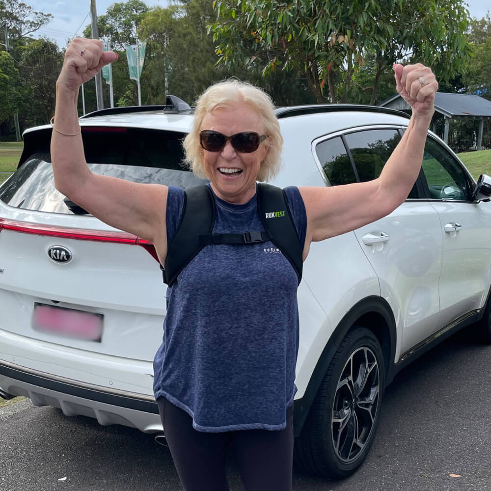 Person with arms raised in front of a white car wearing a rukvest weighted vest