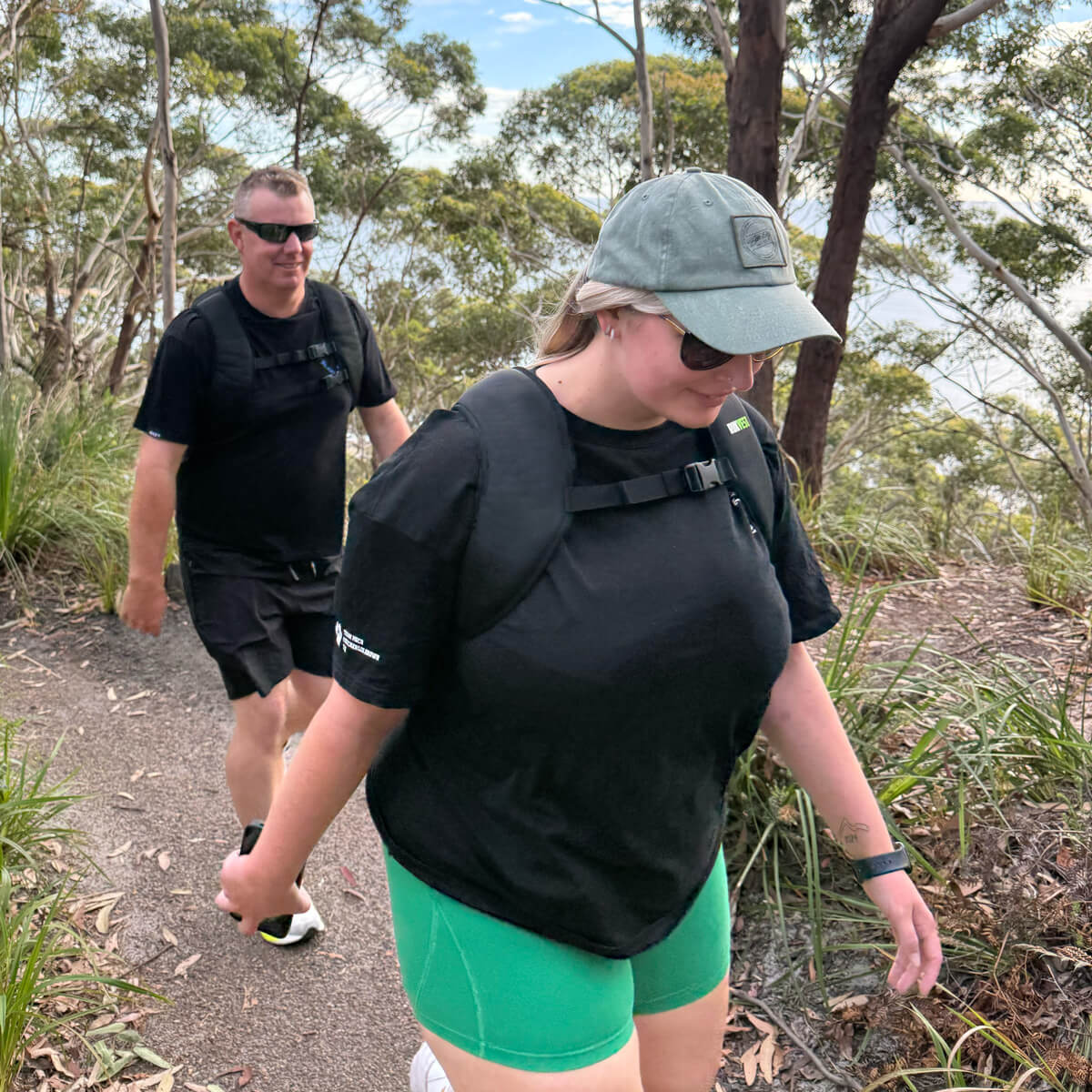 Two people rucking with a RUKVEST on a trail with trees in the background