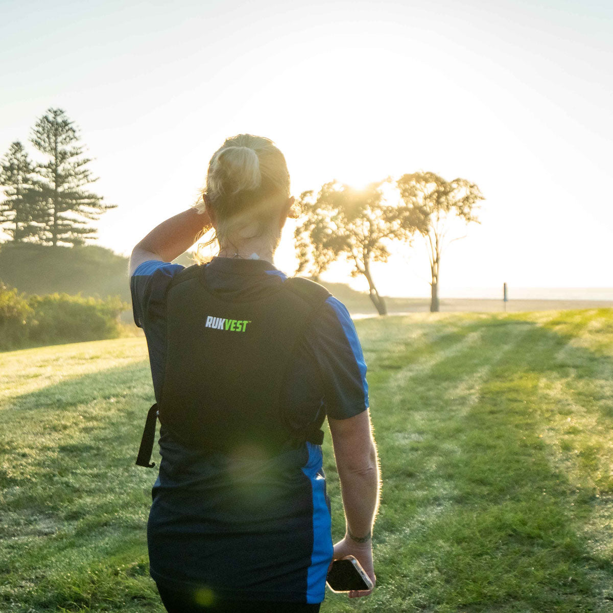 Woman walking across a grassy park at sunrise wearing a RUKVEST