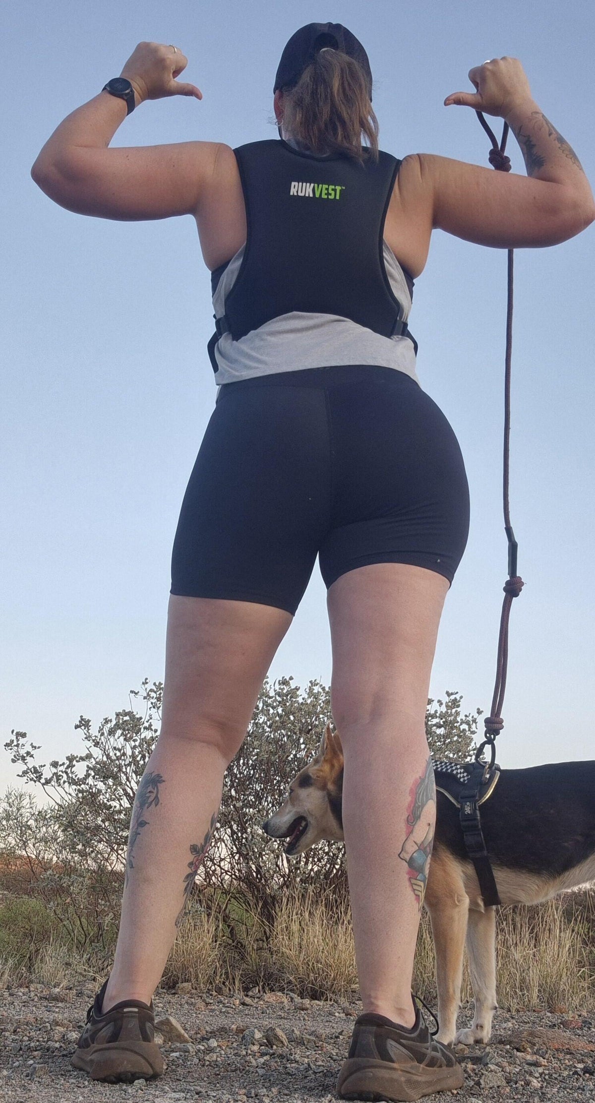 Jess S., a RUKVEST customer, flexing on a sunny hilltop walk in her vest