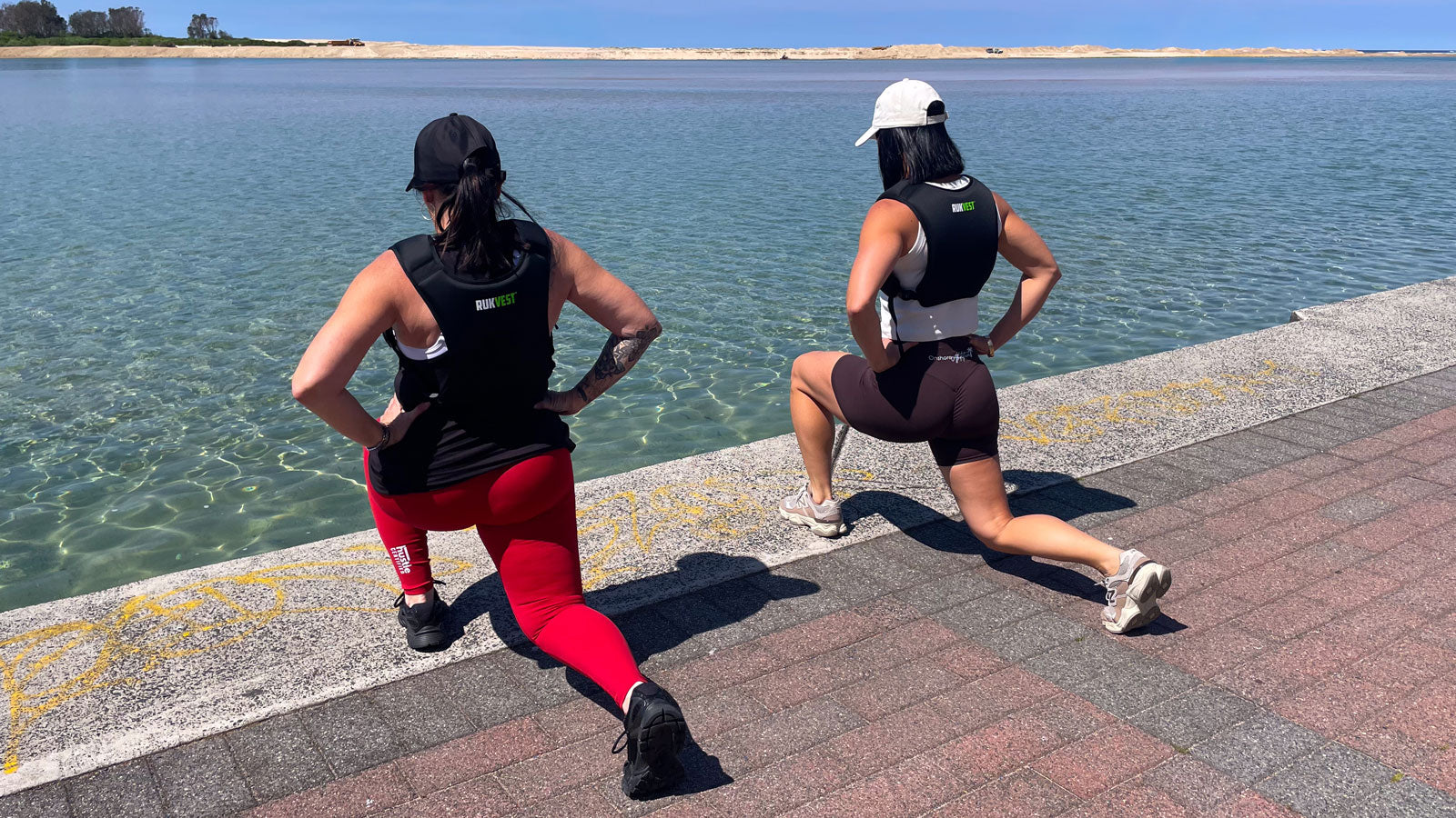 Two women doing a weighted workout by a waterfront wearing RUKVESTs